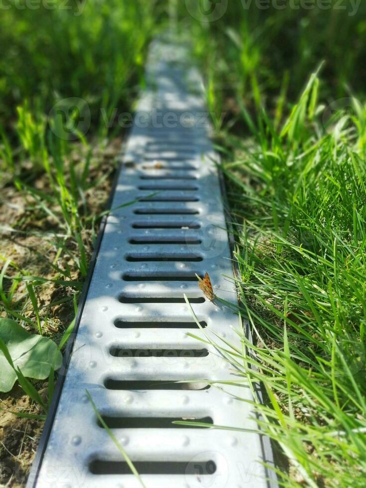 drainage systems. metal construction from the roof - sewer and grate on the ground for draining water closeup. sunny day, green grass photo