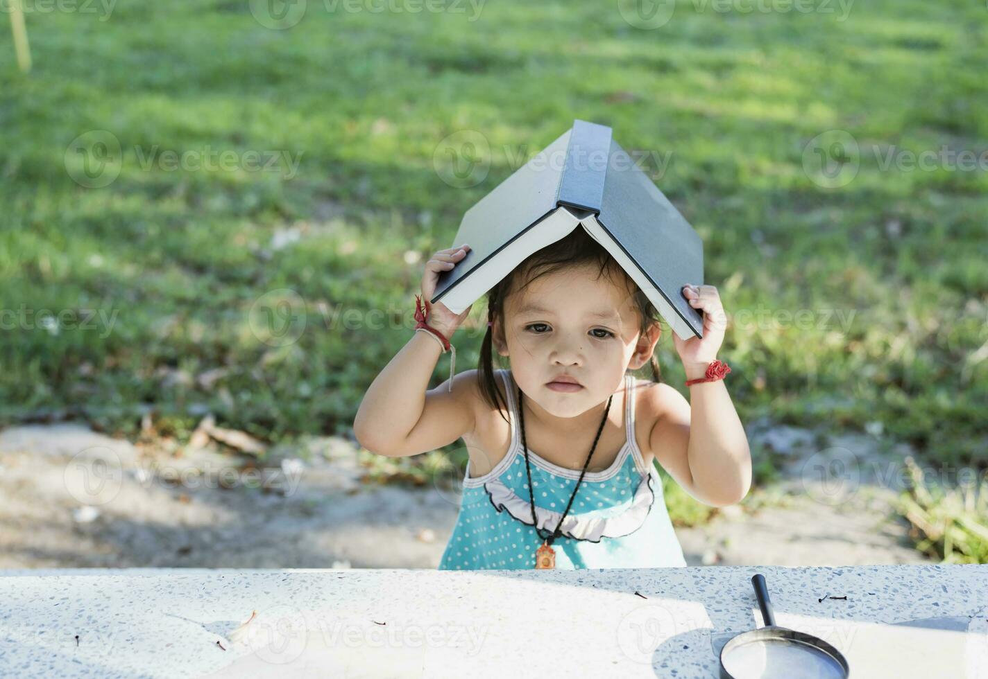 Asian schoolgirl sitting at the table and holding an open book above her head. Back to school concept. photo