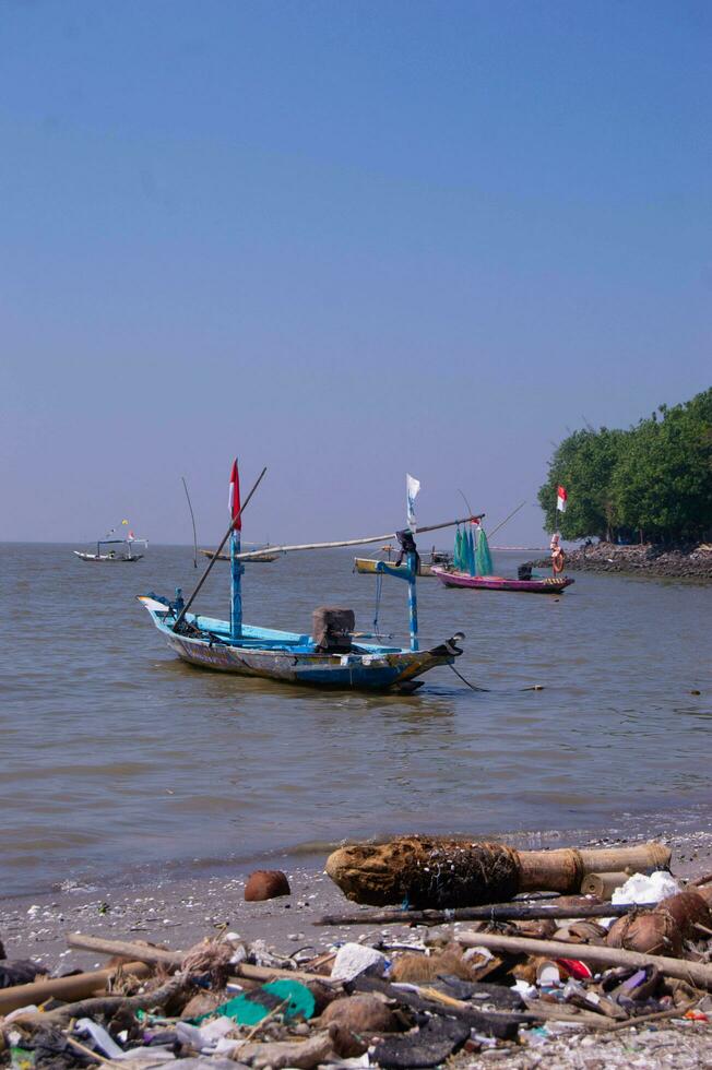 surabaya, indonesia, 2022 - Kenjeran Beach with garbage piled up with fishing boats leaning on it photo