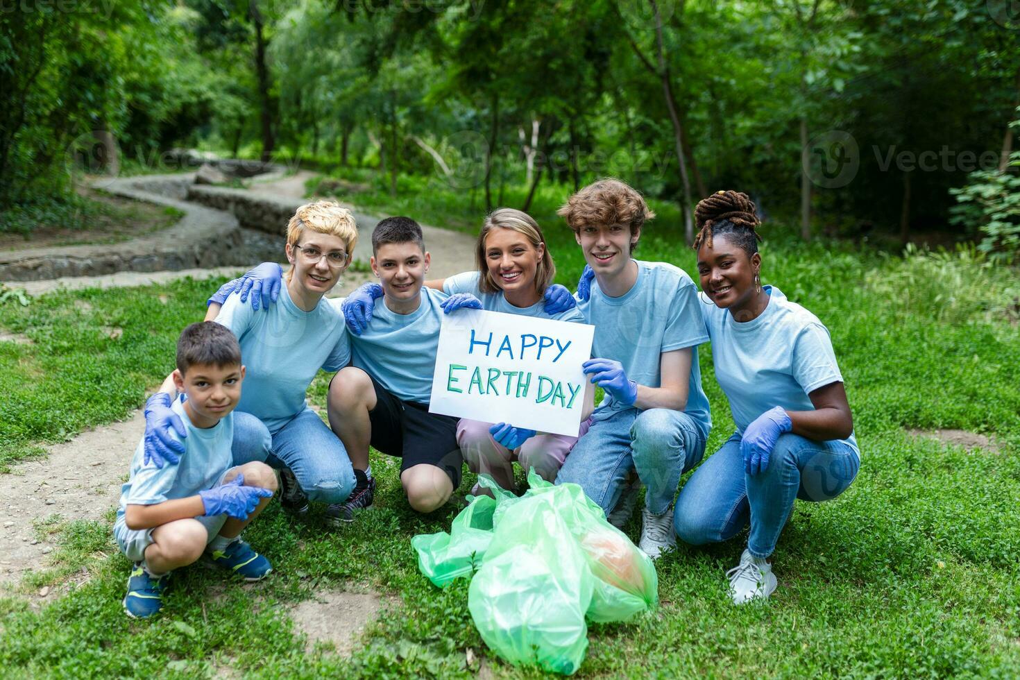 diverso grupo de personas cosecha arriba basura en el parque voluntario comunidad servicio. contento internacional voluntarios participación cartel con 'feliz tierra día' mensaje. foto