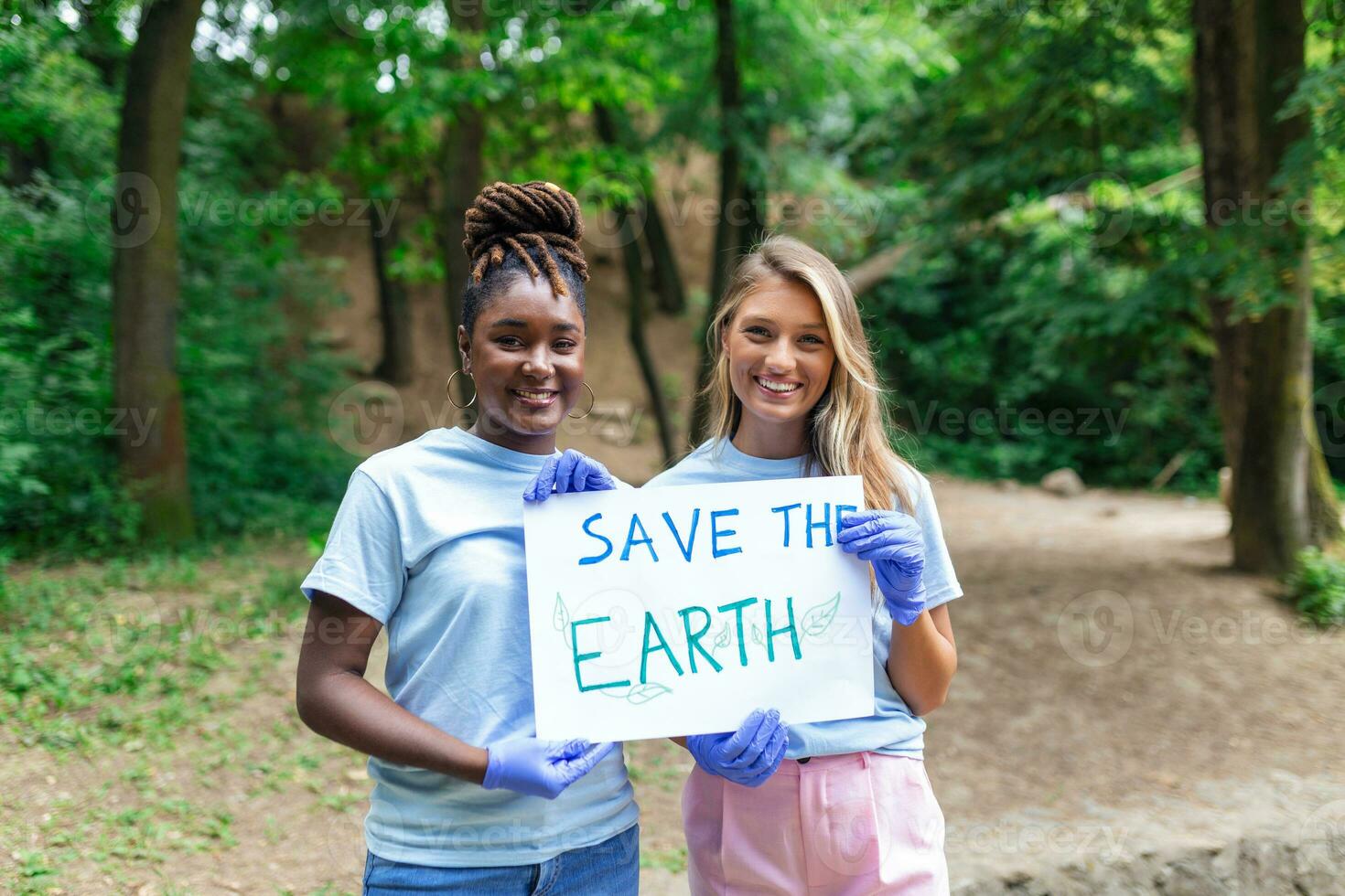 Diverse Group of People Picking Up Trash in The Park Volunteer Community Service. Happy international volunteers holding placard with 'Save the Earth' message. photo