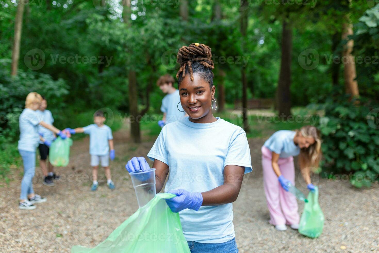 A group of creative young volunteers collect garbage in the open in a public park. Portrait of a young beautiful African woman holding a garbage bag photo