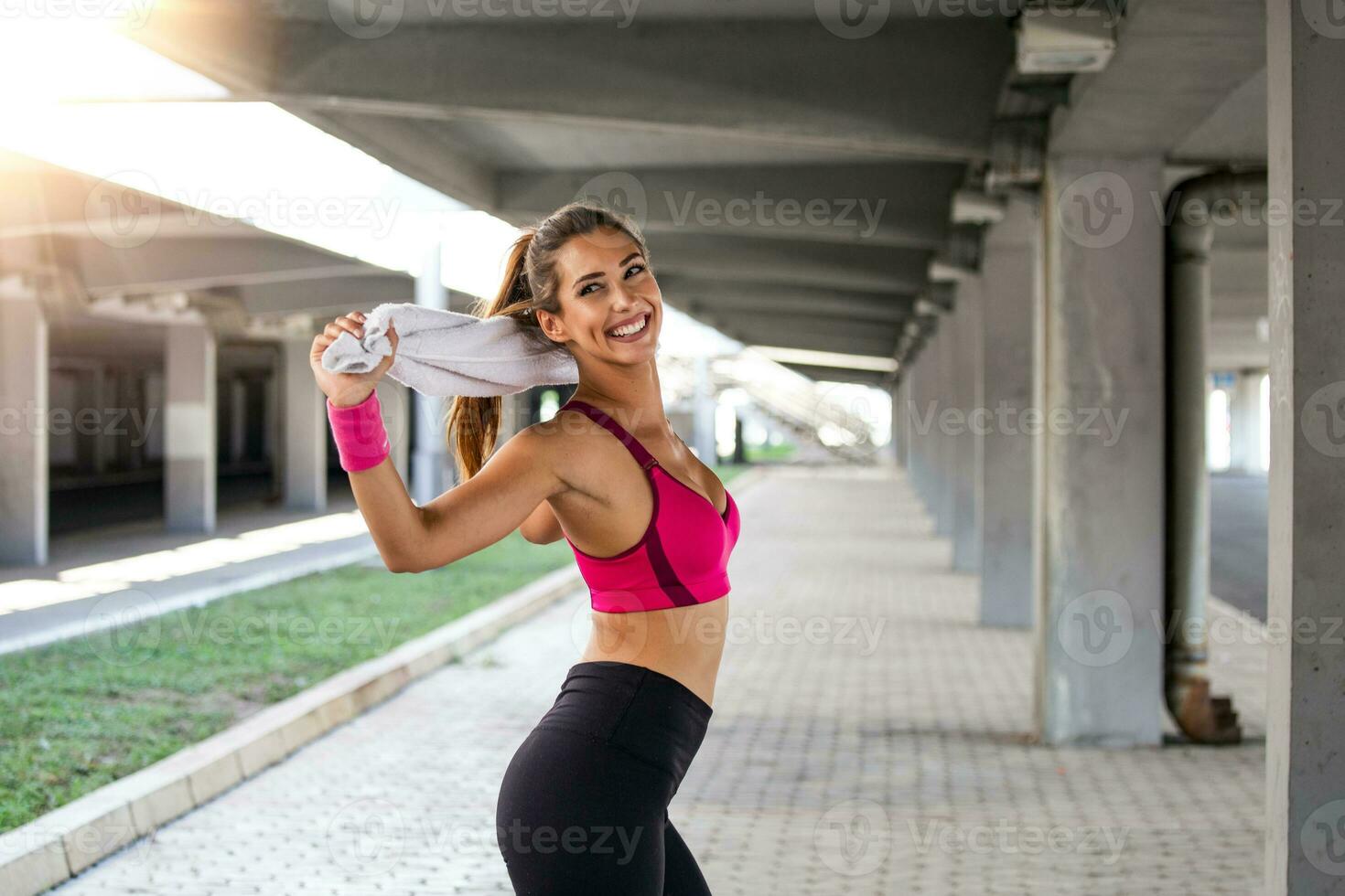 Athletic young woman with towel smiling and streaching. Young sporty woman training. Woman Doing Workout Exercises On Street . Fit girl streaching before active fitness training photo