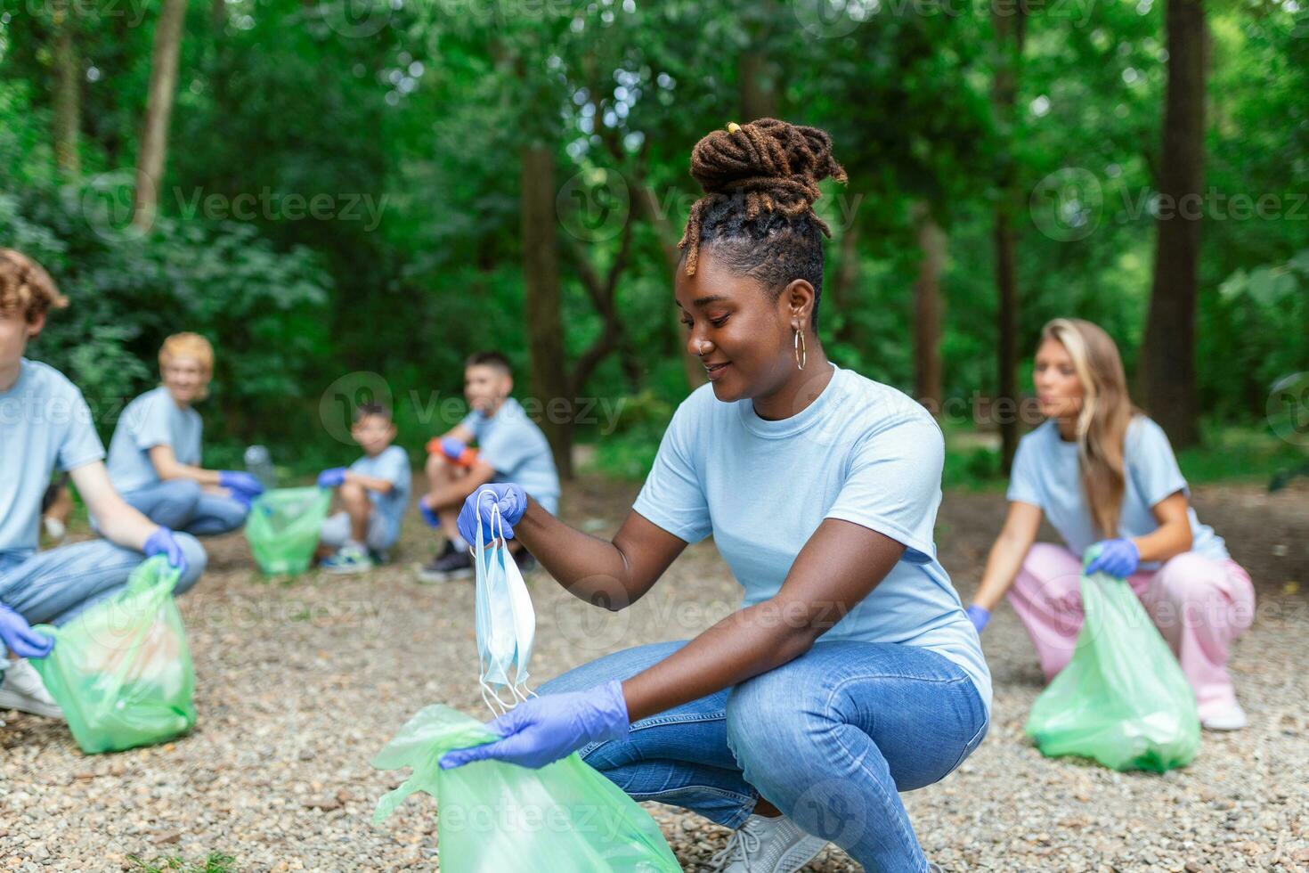 A group of people are cleaning together in a public park, protecting the environment. Woman in the foreground with a garbage bag in her hand cleans the park photo