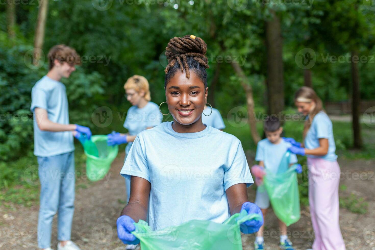 Portrait of beautiful woman with small group of volunteers on background with gloves and garbage bags cleaning up city park - environment preservation and ecology concept. All wearing a blue t-shirts photo