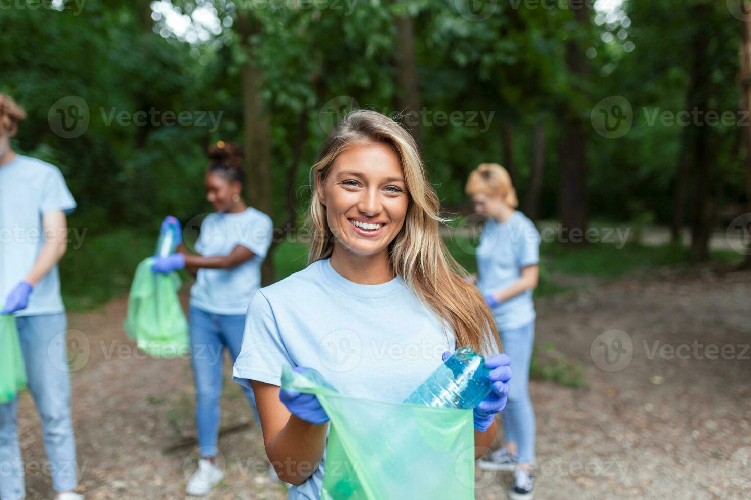 el joven adulto mujer, quien es uno de un diverso grupo de voluntarios, toma hora a sonrisa para el cámara. sostener basura bolso y mirando a cámara foto