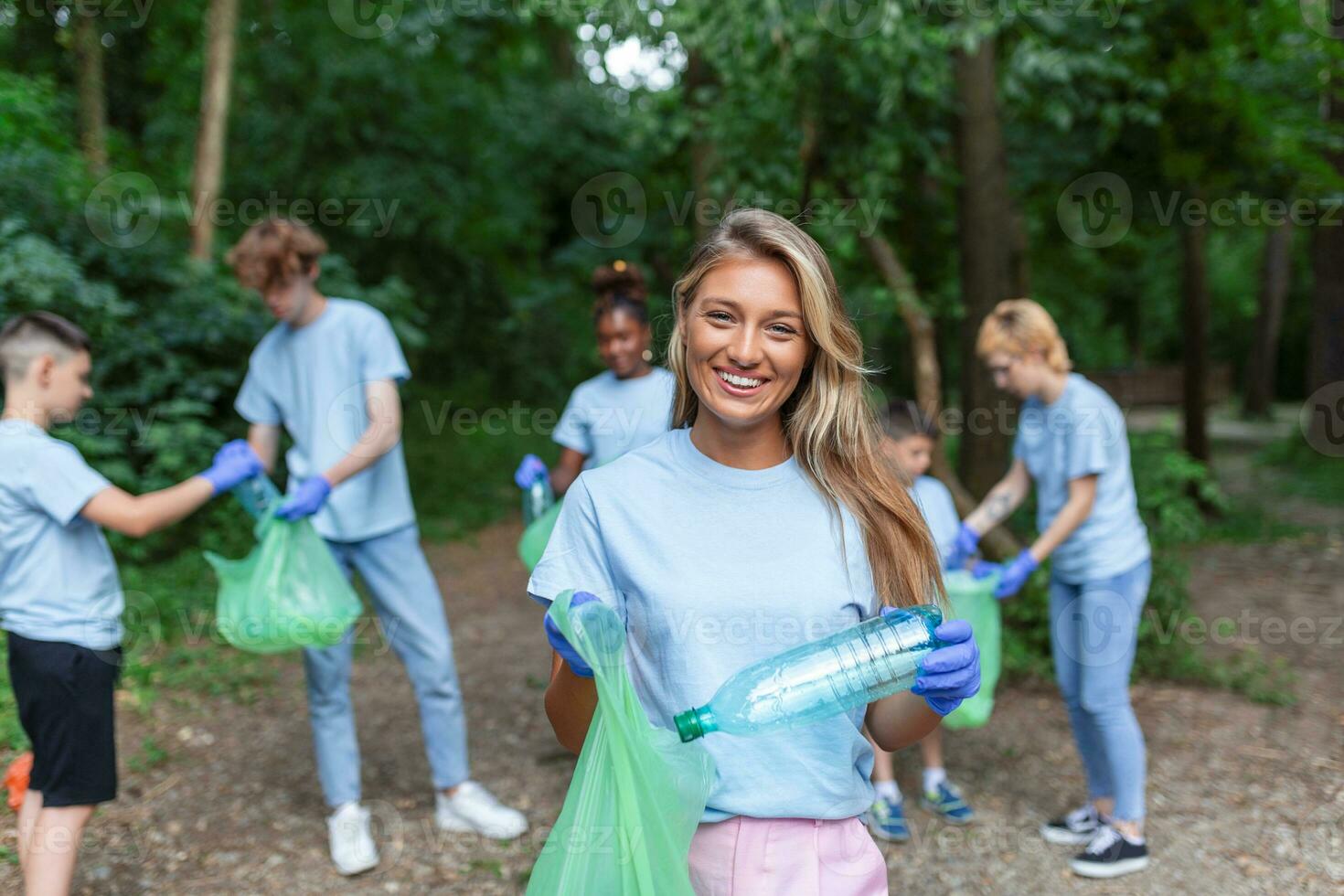 Portrait of beautiful woman with small group of volunteers on background with gloves and garbage bags cleaning up city park - environment preservation and ecology concept. All wearing a blue t-shirts photo