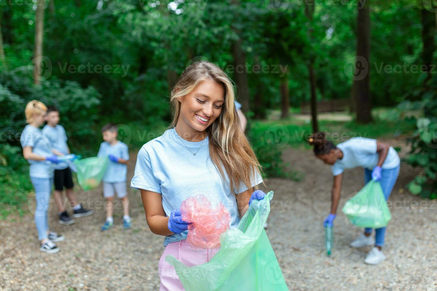 Portrait of beautiful woman with small group of volunteers on background with gloves and garbage bags cleaning up city park - environment preservation and ecology concept. All wearing a blue t-shirts photo