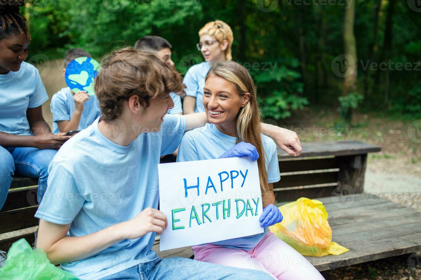 Female and male hands hold a piece of cardboard with the words Happy Earth Day. Happy and satisfied volunteers in nature clean and help maintain the environment. photo