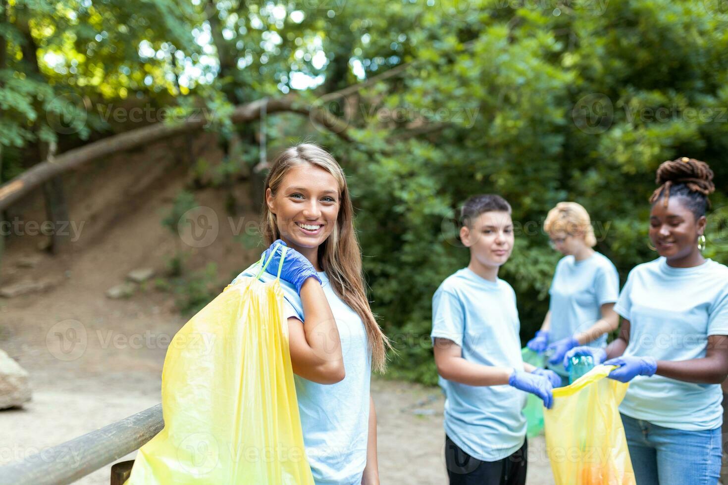 Happy community service people cleaning up local park. They have a trash bag and are filling is with trash they have found in the park. Their are two knealing down and two others behind them photo