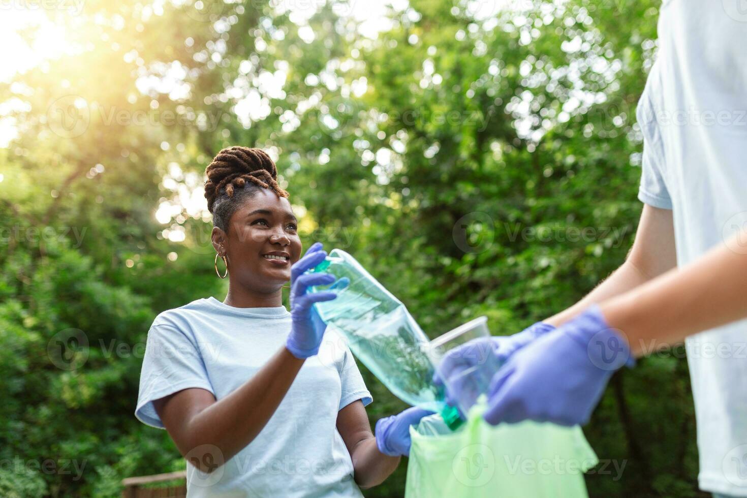 Two smiling diverse young male volunteers putting trash in garbage bags during a community cleanup day in a field photo