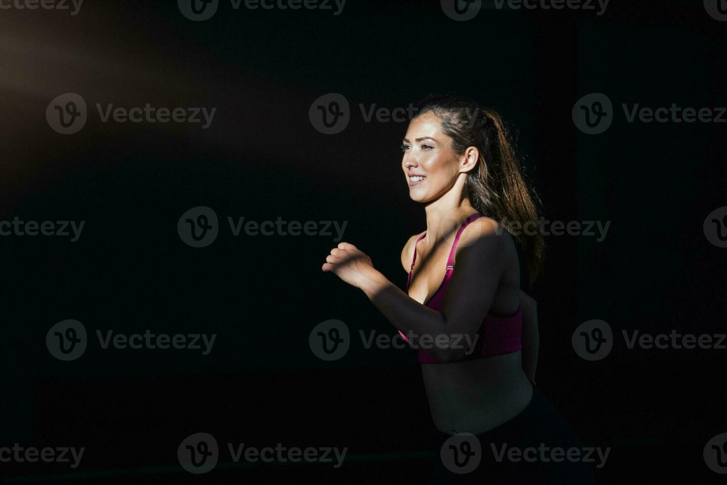 Young woman with fit body running against dark background. Female model in sportswear exercising outdoors.Woman Doing Workout Exercises On Street. photo