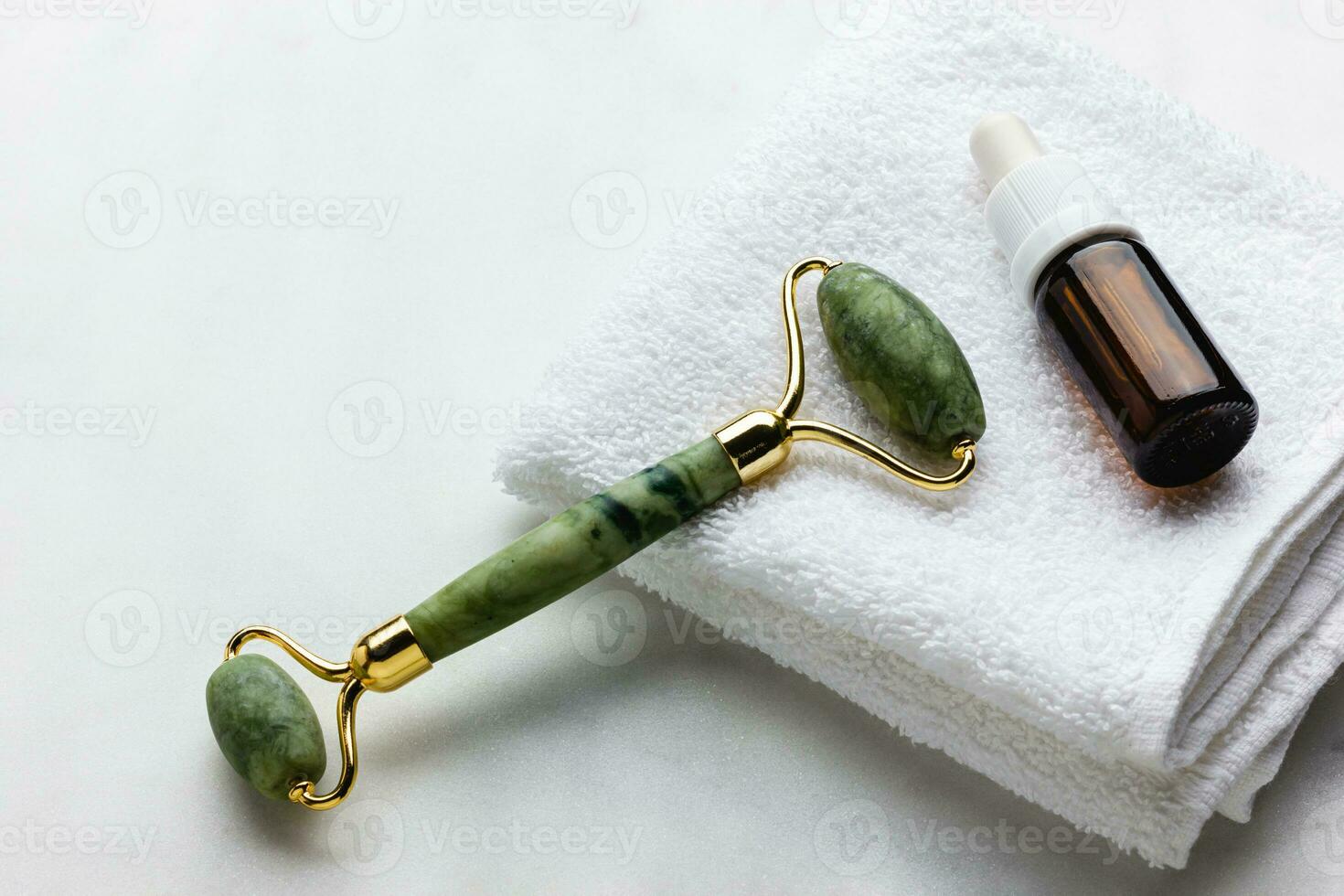 Green jade roller massager for face on white marble. photo