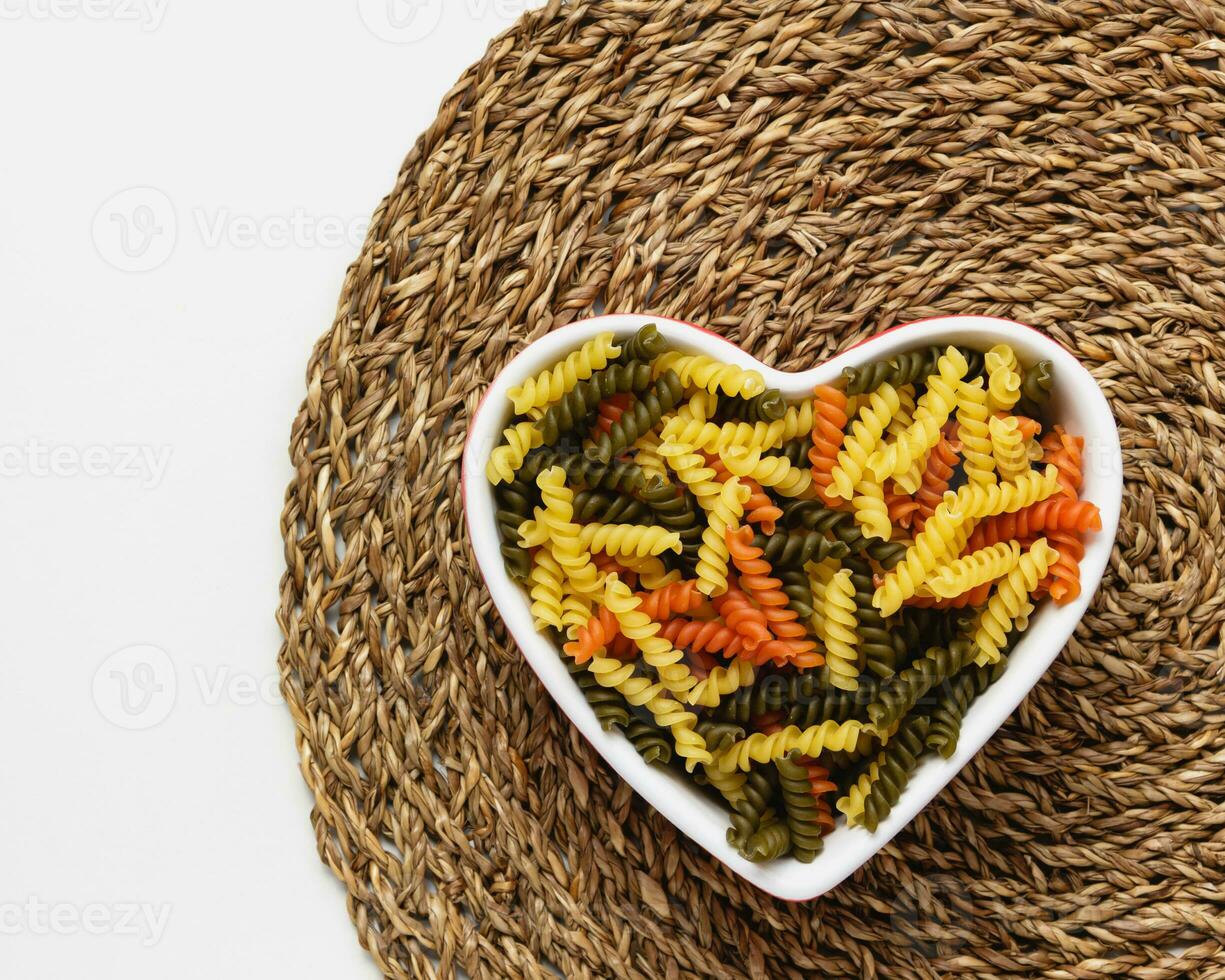 Raw pasta torti in heart bowl. photo