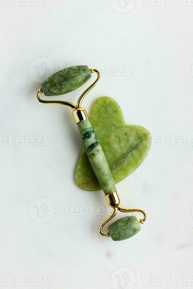 Green jade roller massager for face on white marble. photo