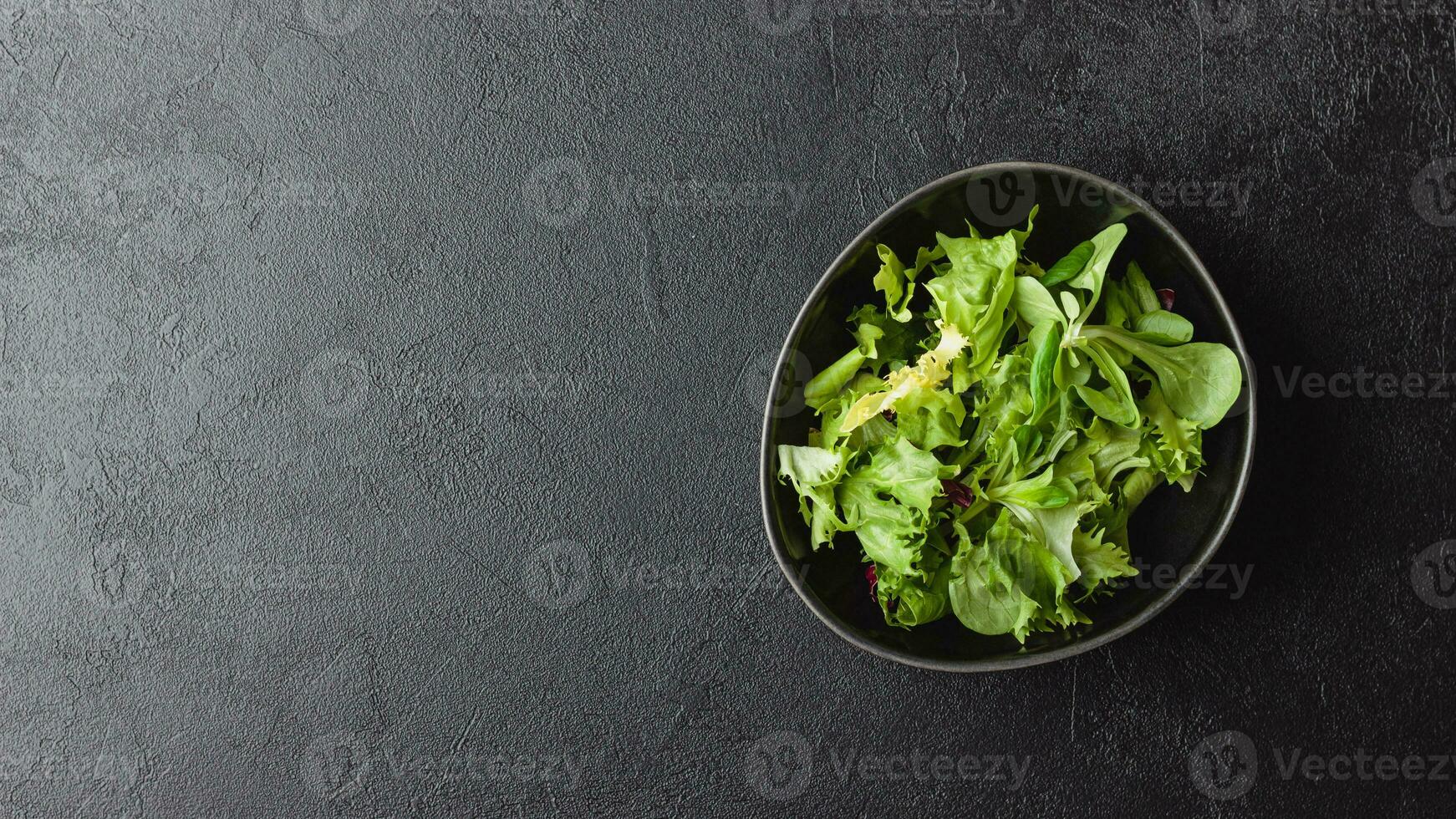hojas de ensalada verde en un tazón sobre una mesa negra. foto