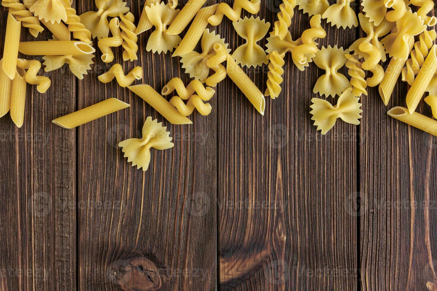 Different kinds of raw pasta texture with copy space on wooden background. photo