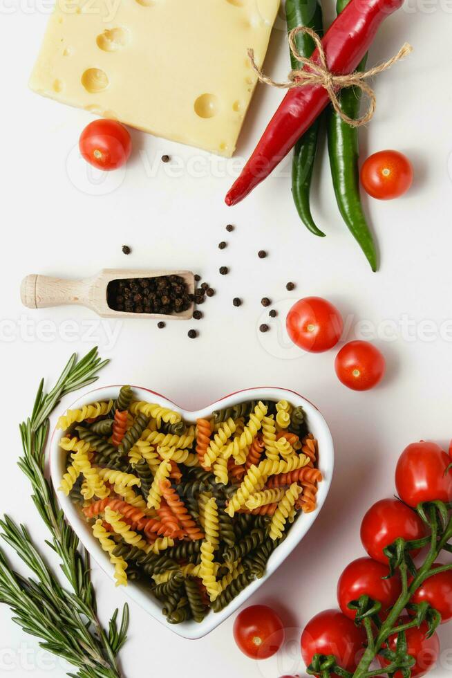 Raw pasta torti in heart bowl with cherry tomatoes, cheese, rosemary, chilli and allspice. photo