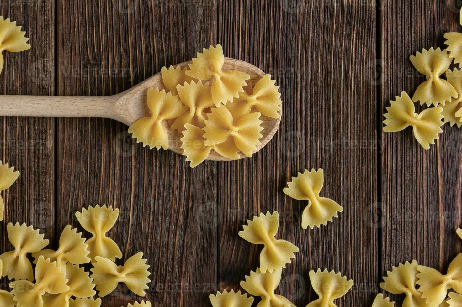 Raw pasta farfalle on spoon on wooden background. photo
