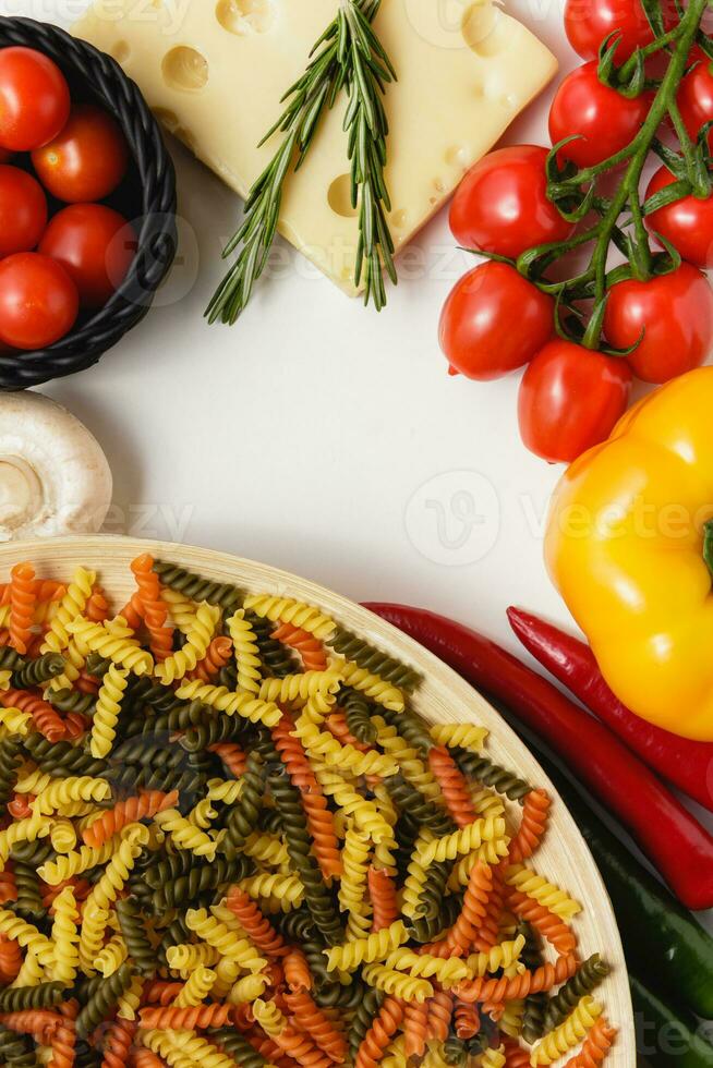 Raw pasta fusilli on plate with cherry tomatoes, cheese, rosemary, paprika and chilli. photo