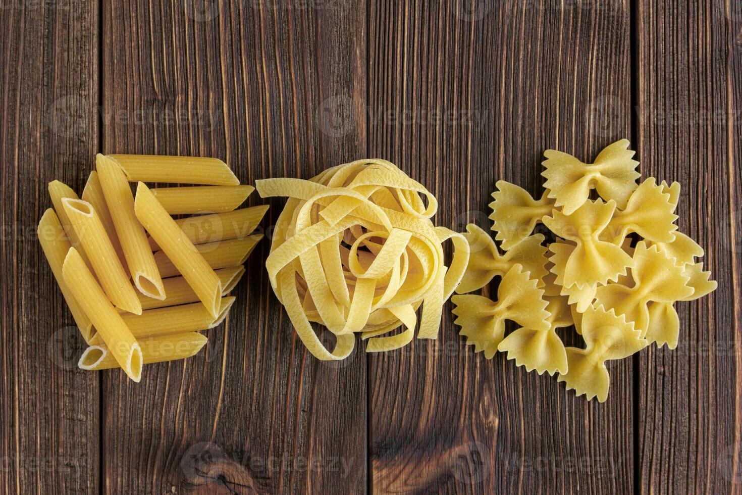 Different kinds of raw pasta on wooden background. photo