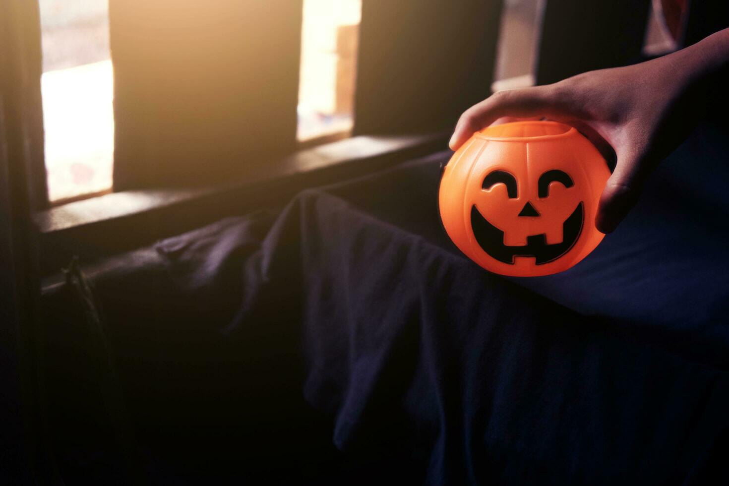 Scare hand holdung Halloween pumpkin head on black clothes in natural shadow and sunlight. Halloween holiday concept. photo