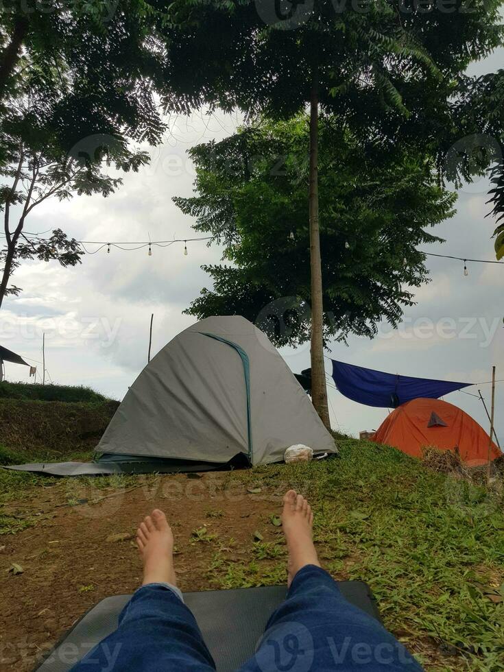 Some tents camping on a hill. Ash and orange colored tents. There is also a hammock attached to the tree. photo