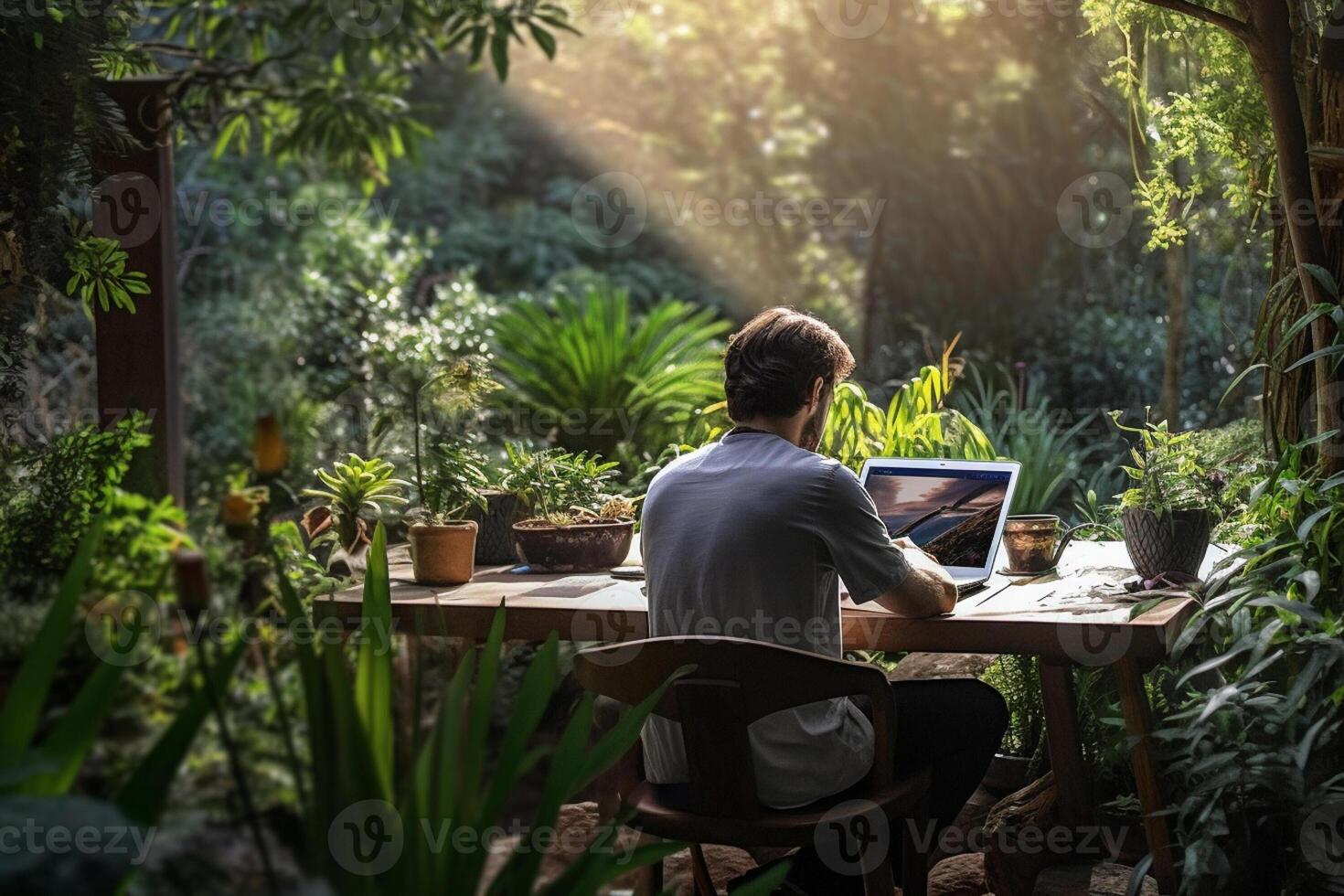 a man sitting on a table outside using a laptop in a garden with photo
