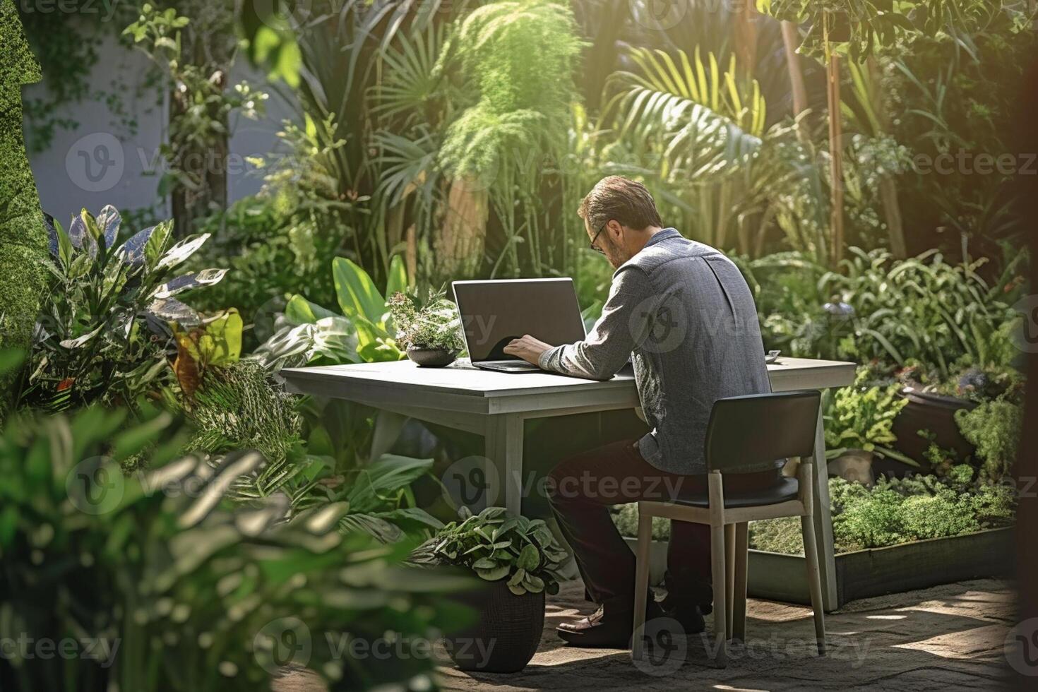 a man sitting on a table outside using a laptop in a garden with photo