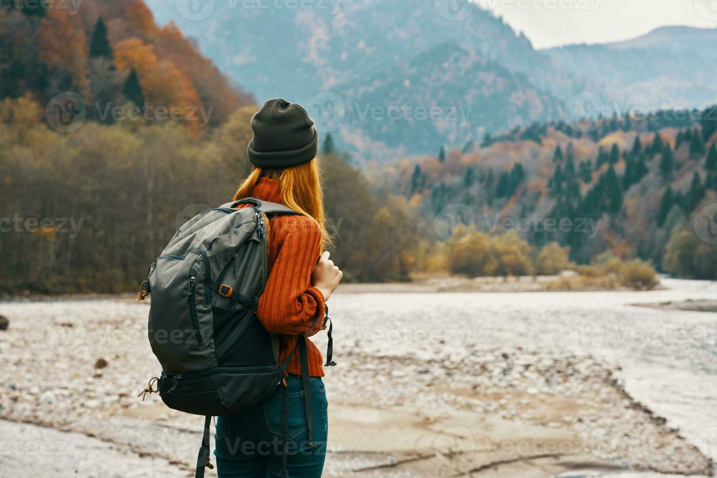 woman travels in the mountains in autumn near the river in nature with a backpack back view photo