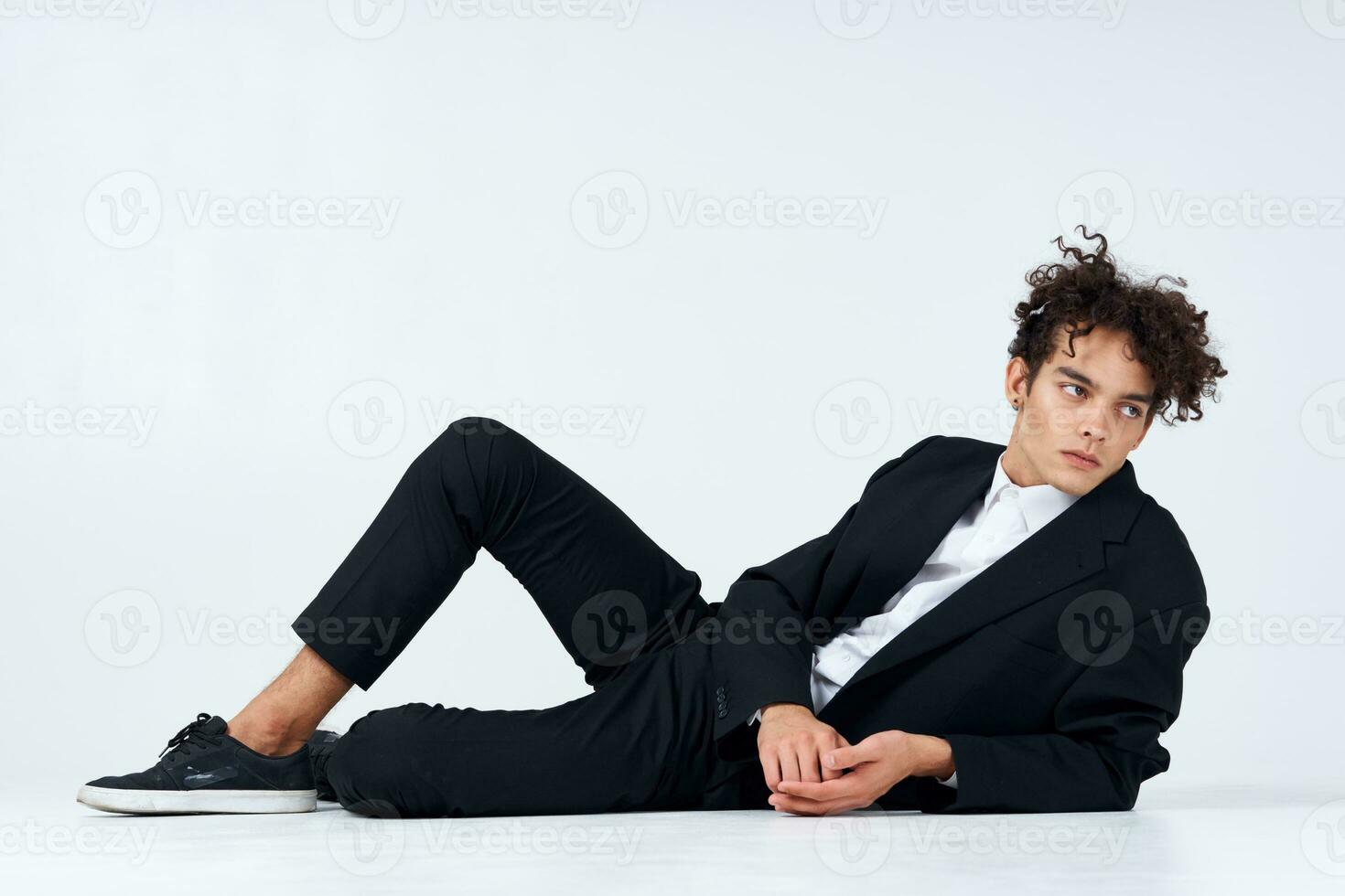 a guy a teenager in a suit lies on the floor and sneakers curly hair light background photo