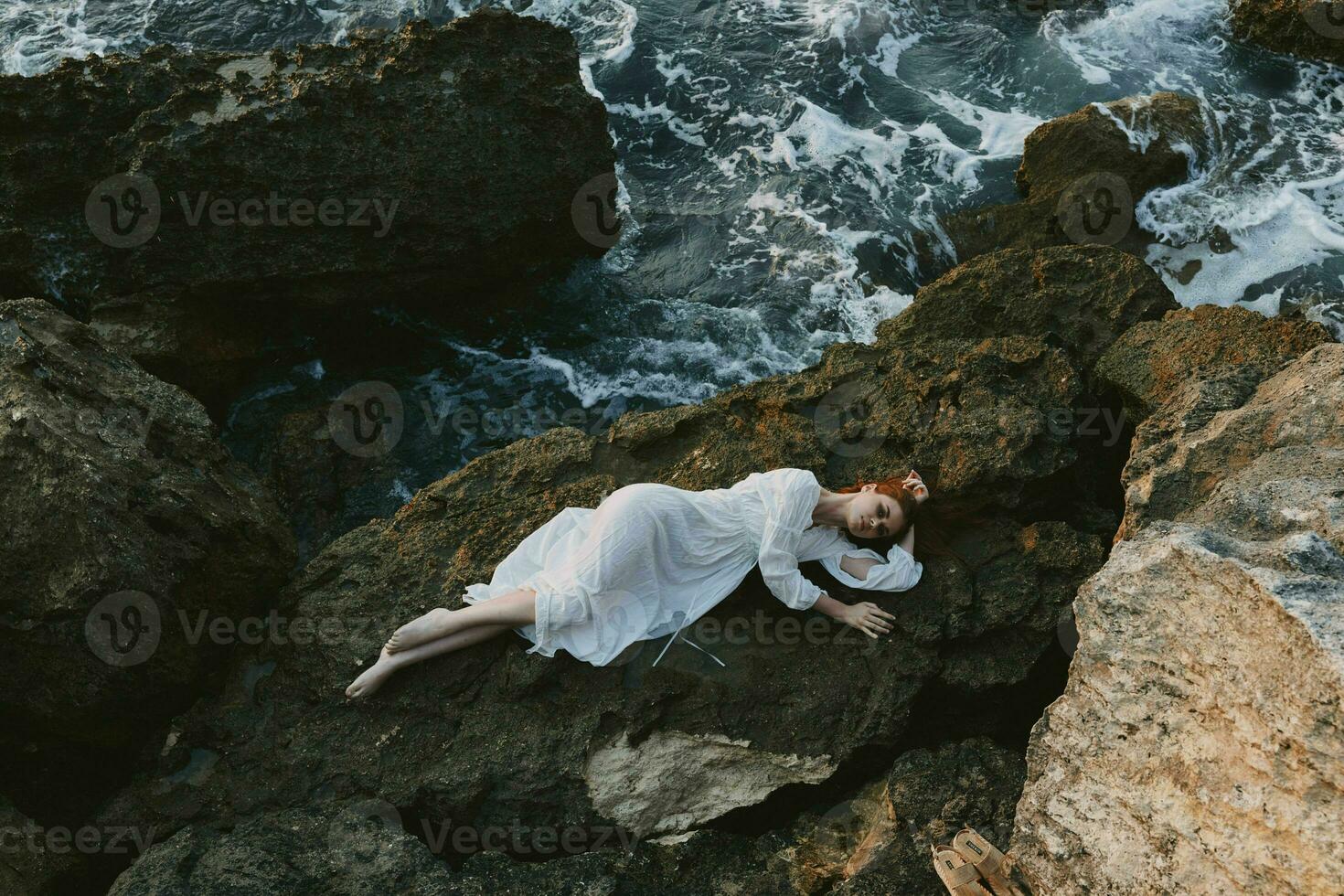 sensual mujer acostado en rocoso costa con grietas en rocoso superficie paisaje foto