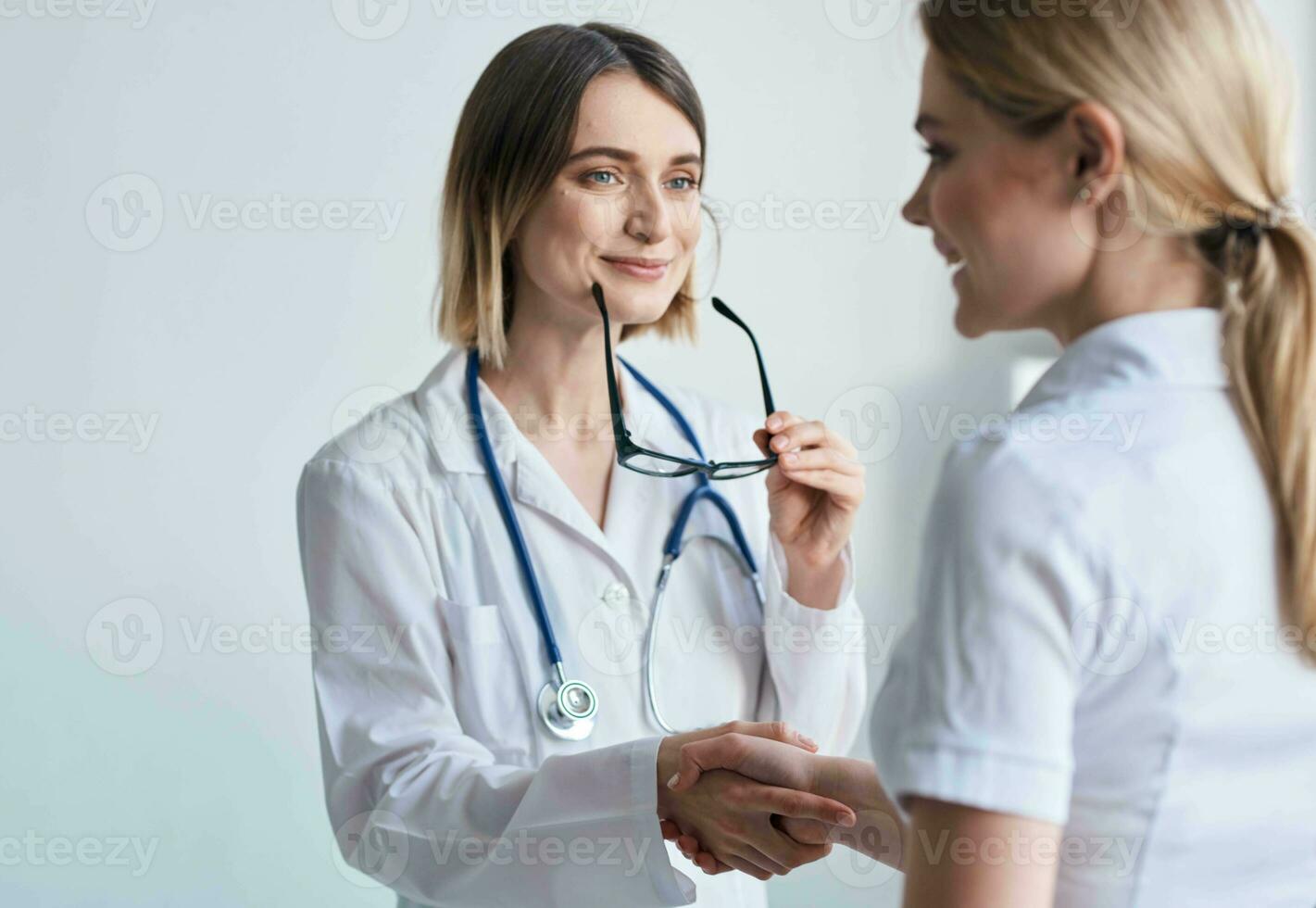 beautiful woman doctor with stethoscope shaking hands with female patient photo