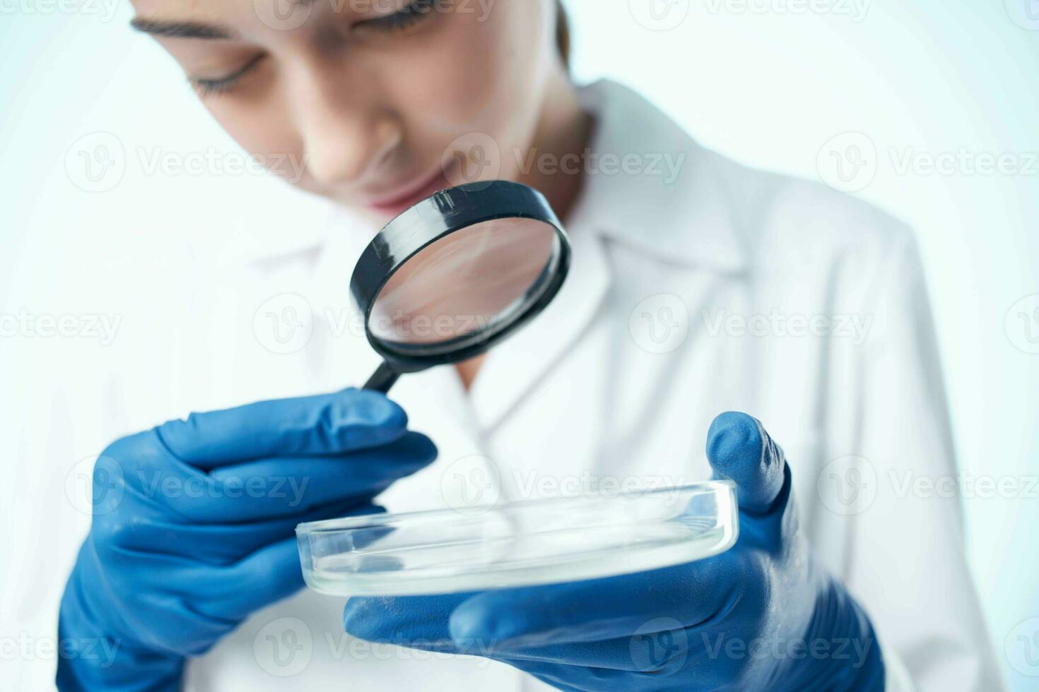 hembra laboratorio asistente en un blanco Saco mirando mediante un aumentador vaso profesional investigación foto