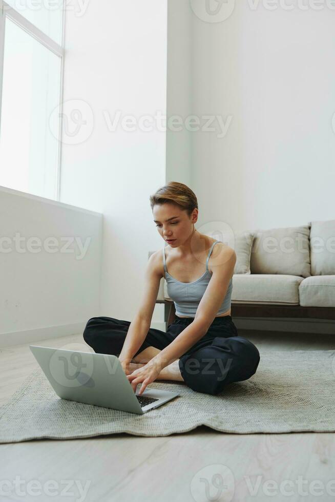 Freelance woman with laptop and phone works from home sitting on the floor in her home clothes with a short haircut, free copy space photo