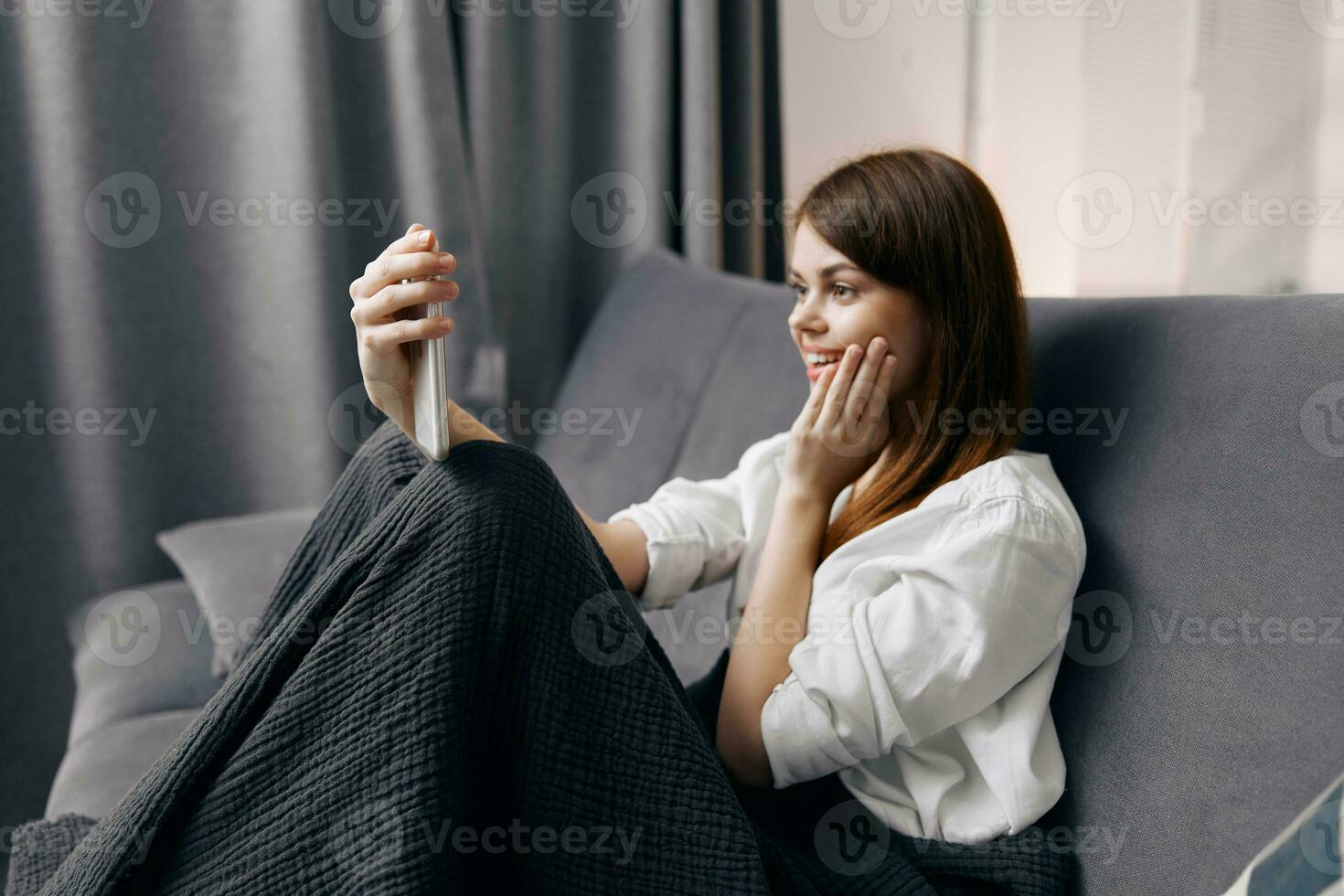 woman on the sofa with a blanket on her lap and a mobile phone in her hand photo