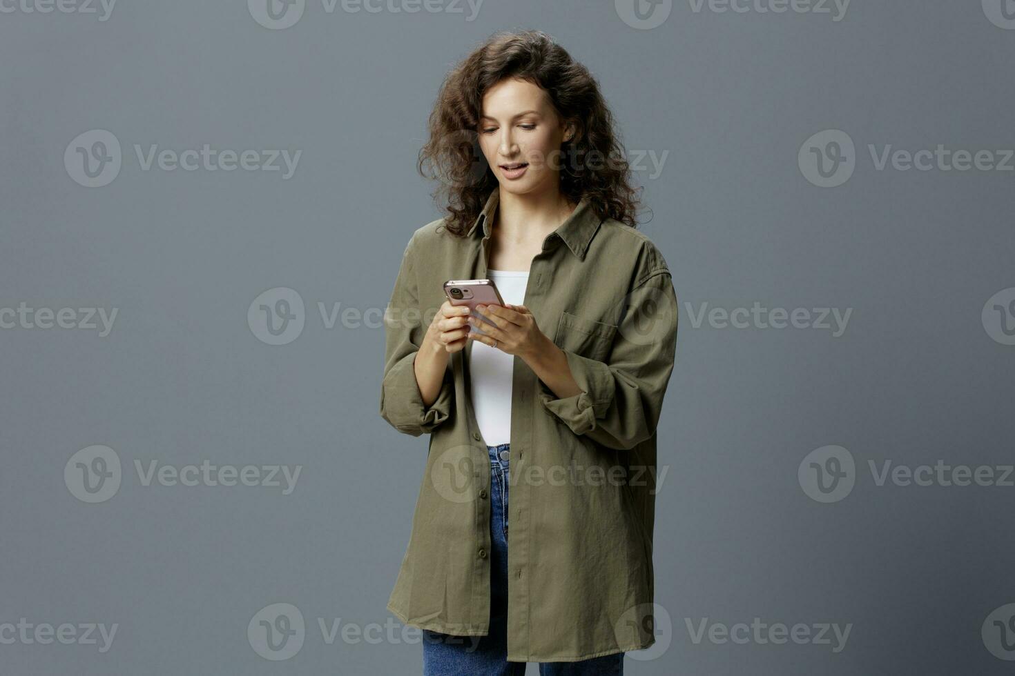 Shocked excited confused curly beautiful woman in casual khaki green shirt get shock info from message using phone posing isolated on gray blue background. Social Media Influencer concept. Copy space photo