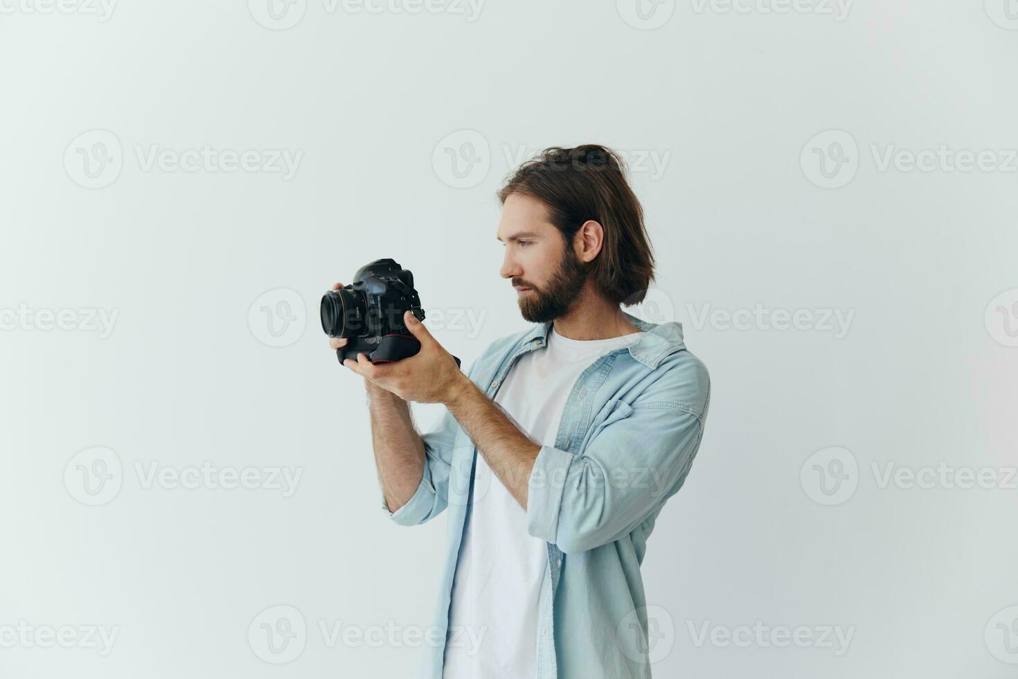A male hipster photographer in a studio against a white background looks through the camera viewfinder and shoots shots with natural light from the window. Lifestyle work as a freelance photographer photo