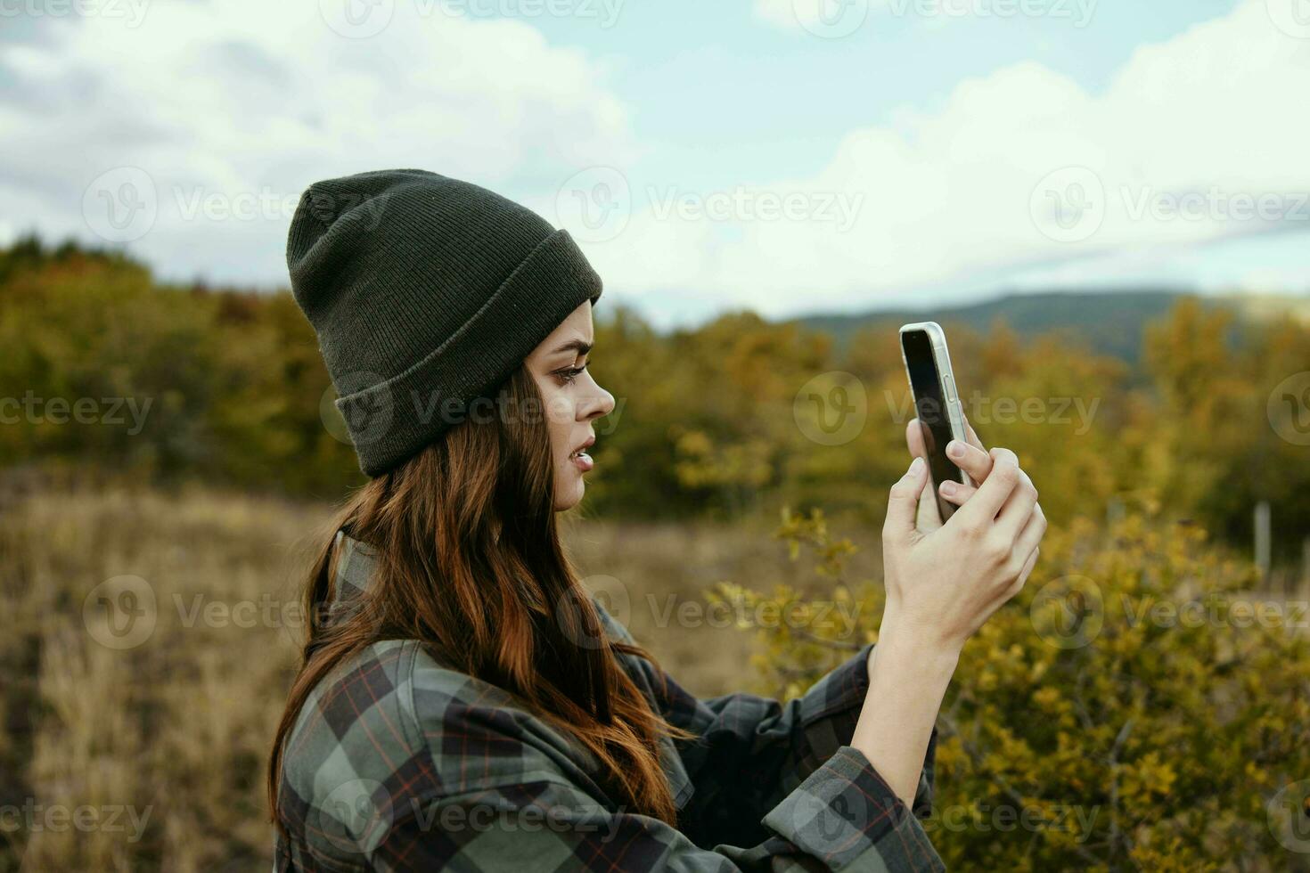 Woman in nature with a mobile phone and a checkered shirt hat on her head photo