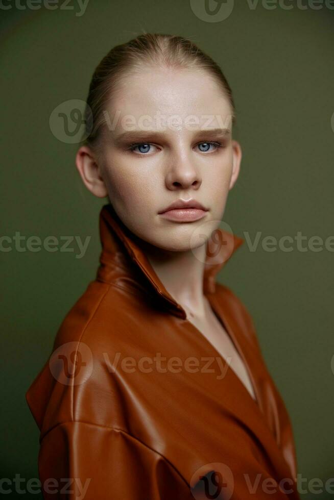 Elegant fashionable young blonde girl with blue eyes with evening makeup in a leather dress looks at the camera posing isolated for banner design. Studio portrait on a green background. Makeup concept photo