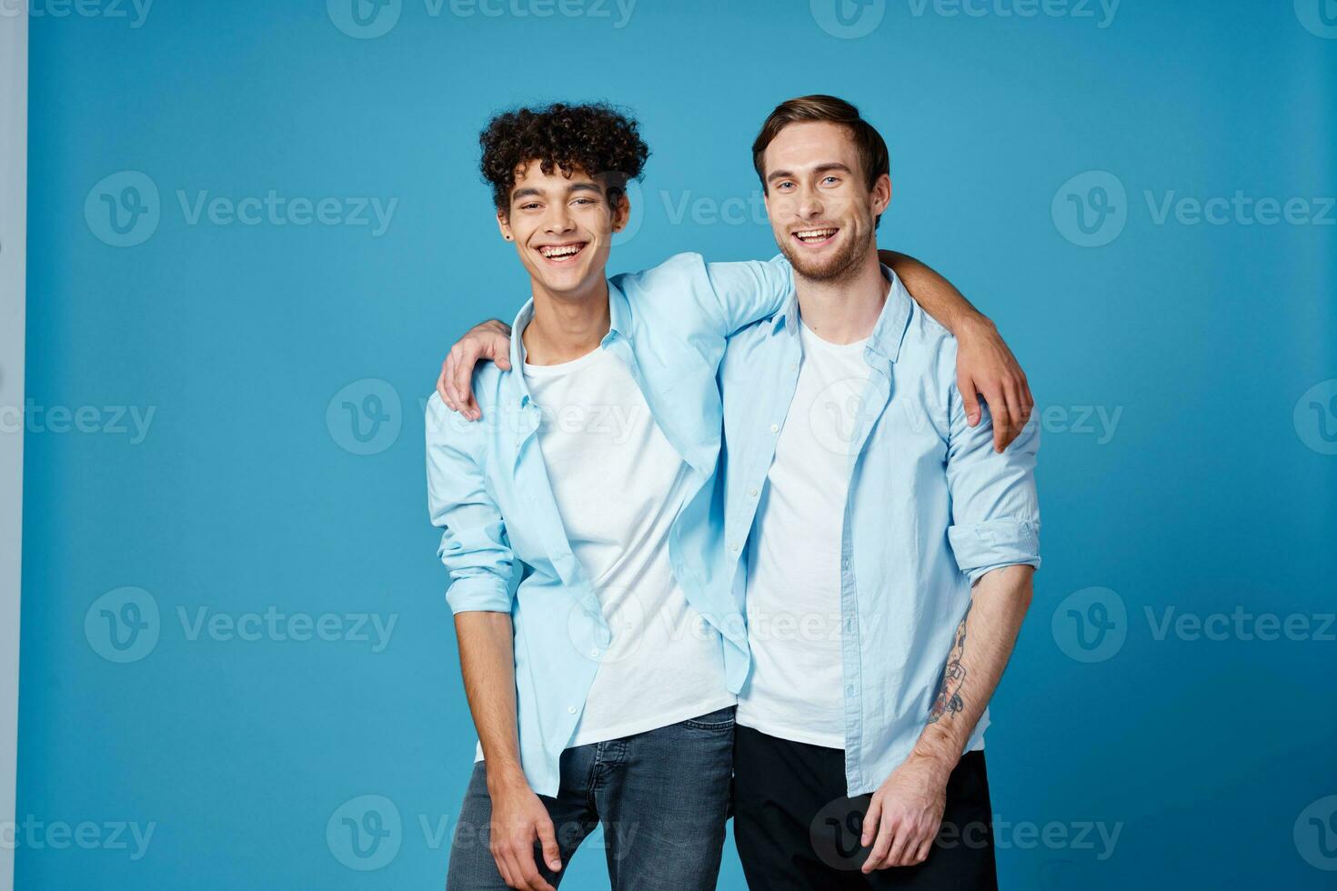 chico con Rizado pelo en un camisa y un camiseta en un azul antecedentes y un joven hombre amigos divertido foto