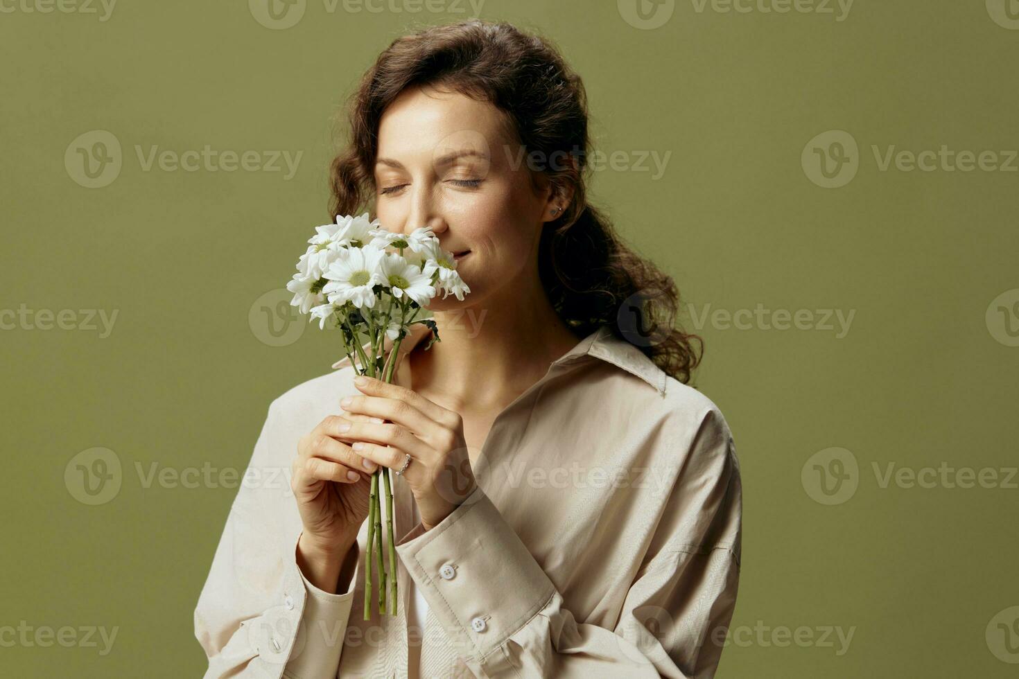 sonriente linda Rizado hermosa hembra en lino casual camisa sostener manzanillas flores cerca cara disfrutando oler posando aislado en terminado aceituna verde pastel antecedentes. naturaleza es belleza concepto. Copiar espacio foto