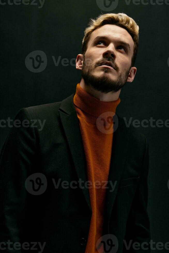 de moda chico en naranja suéter y chaqueta mirando arriba en oscuro antecedentes recortado ver foto