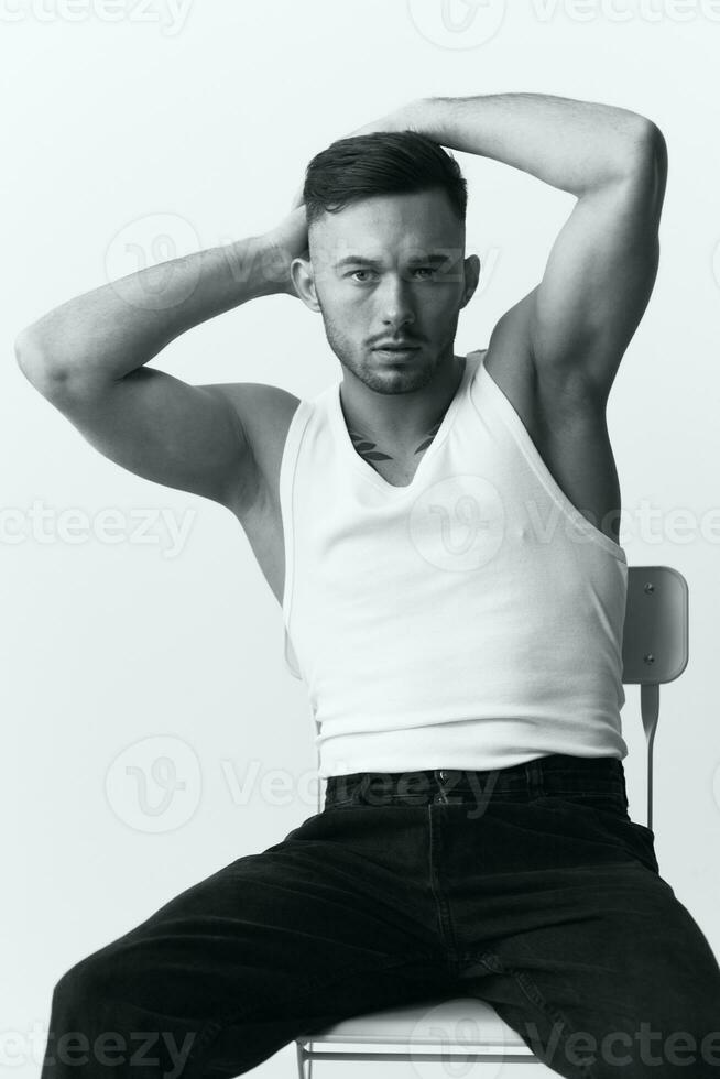 Modelling snapshots. Serious self-confident attractive handsome muscular guy man raise hands up sitting on chair in white studio background. Black and White concept. Copy space photo