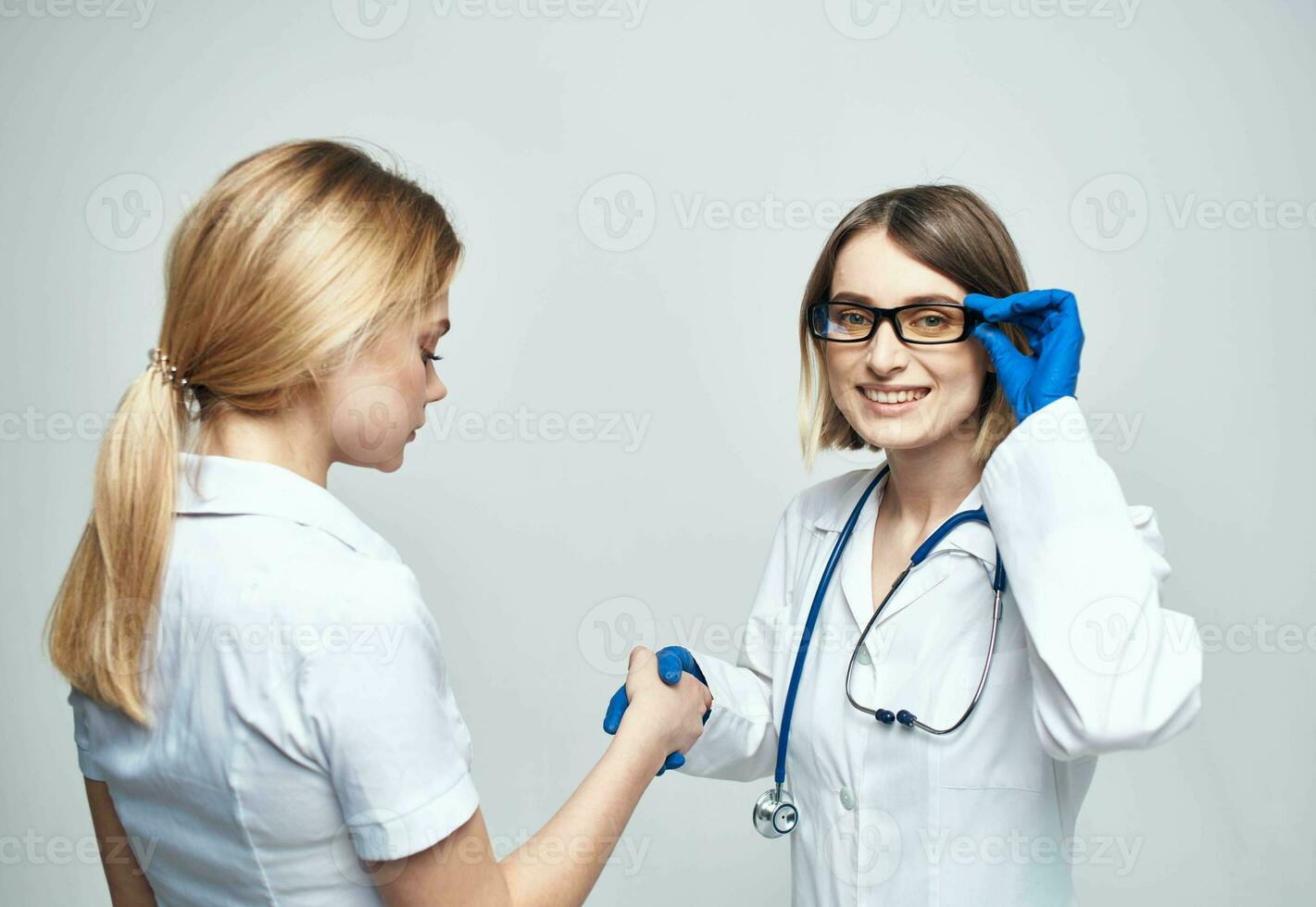 el enfermero batidos manos con el paciente en un ligero antecedentes y azul guantes con un estetoscopio foto