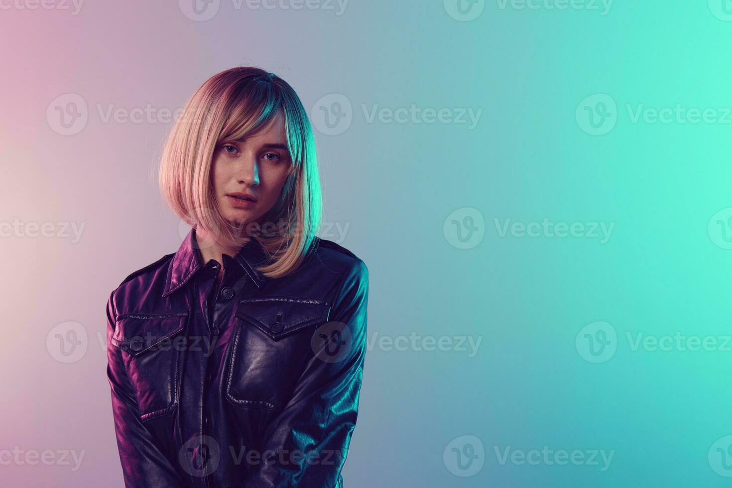Pretty sexy beautiful blonde woman in leather jacket look at camera posing isolated in blue turquoise pink color light studio background. Neon party Cyberpunk concept. Copy space photo