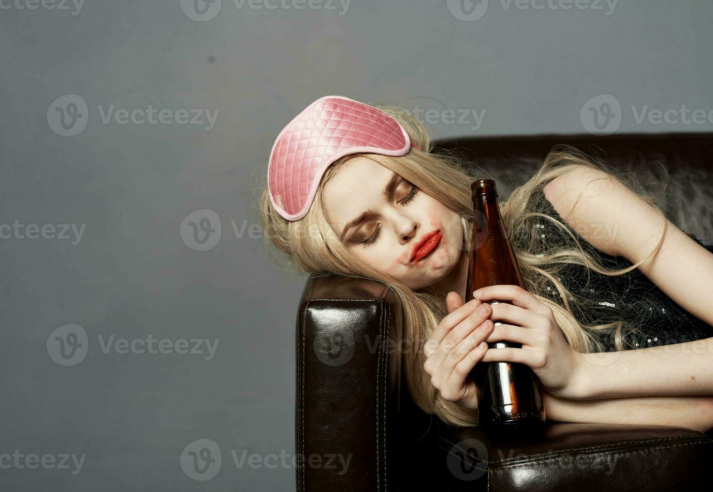 woman with bottle of beer on sofa alcohol addiction sleep mask on head photo