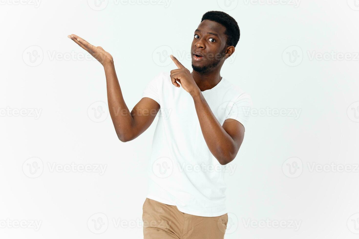 a handsome guy of African appearance gestures with his hands on a light background and points his finger to the side photo