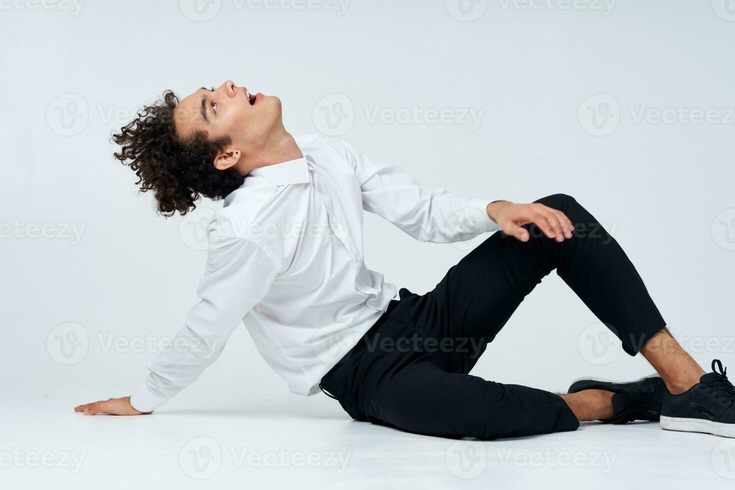 trendy guy with curly hair in a classic suit and sneakers on the floor indoors photography studio photo