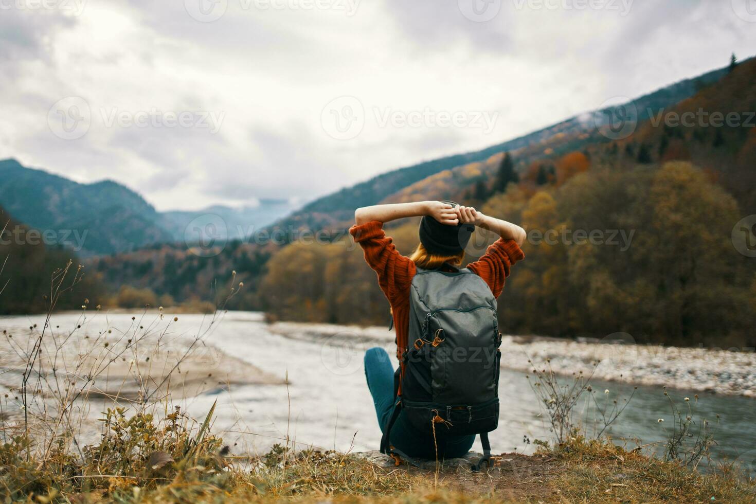 woman traveler with a backpack on her back gestures with her hands and looks at the mountains in the distance photo